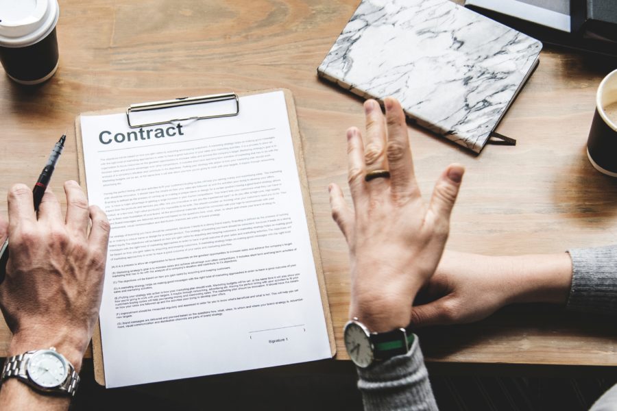 two hands about to sign a contract attached to a clipboard