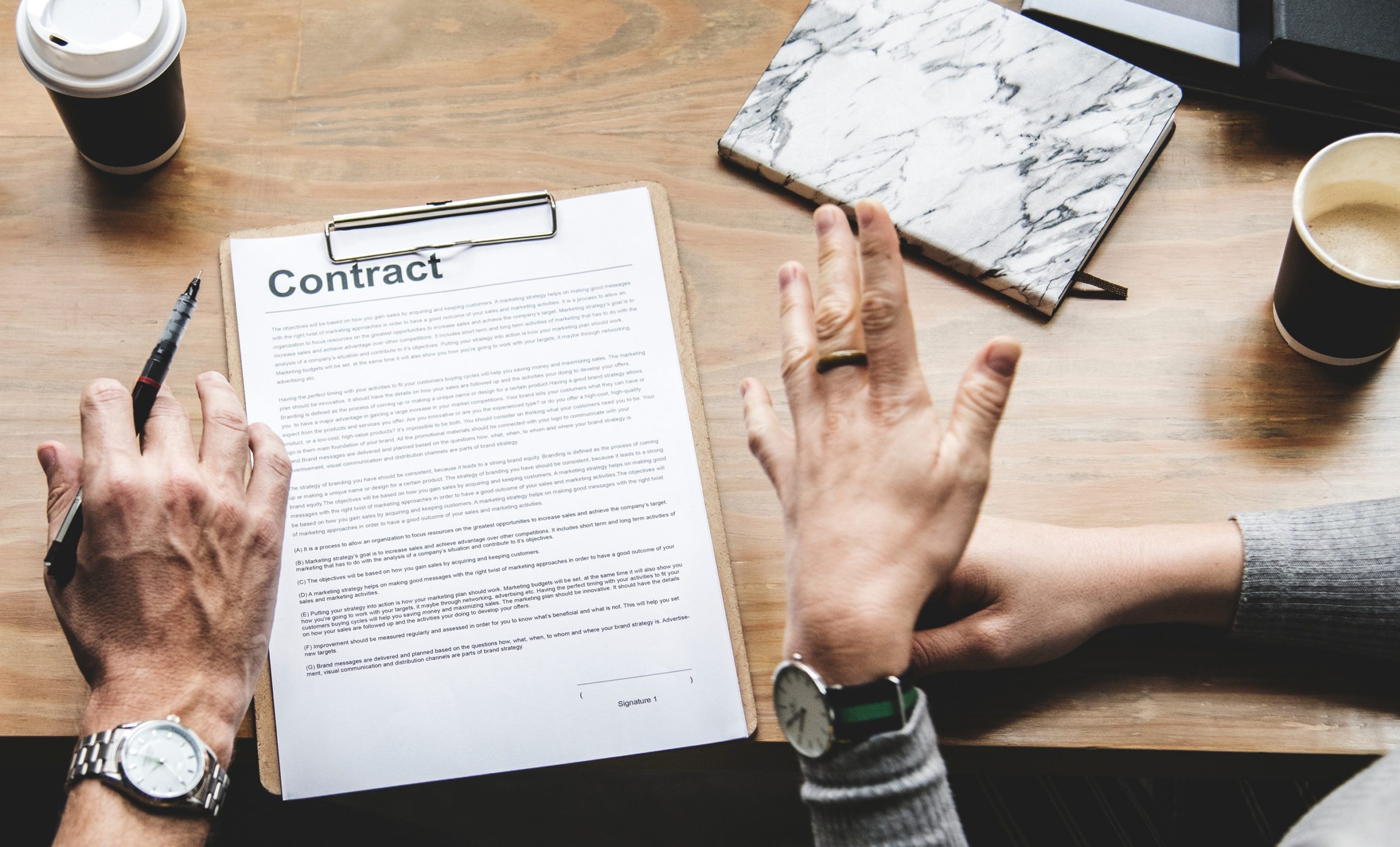 two hands about to sign a contract attached to a clipboard