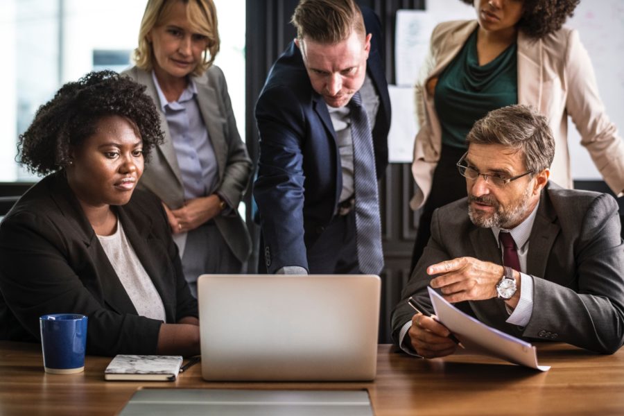 group of business professionals huddled around a laptop