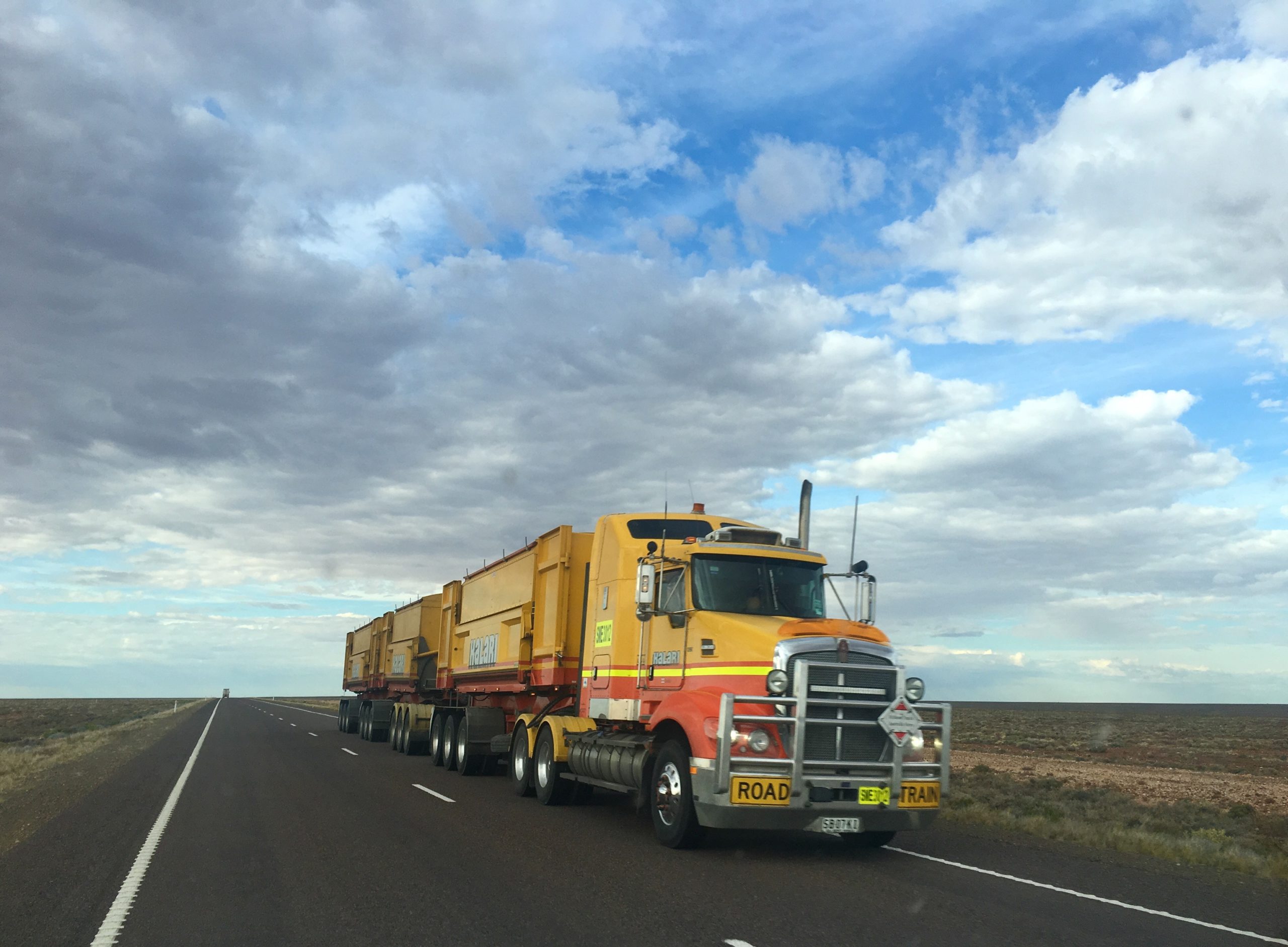 semi truck driving on highway with blue cloudy sky in background