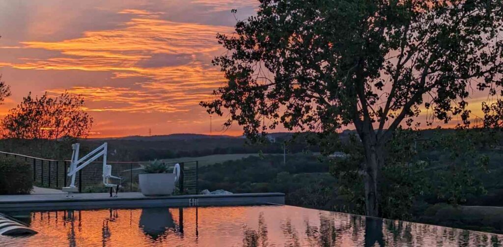 PXL 20231106 234926908 Colorful sunset reflecting in a peaceful infinity pool overlooking hills and trees.