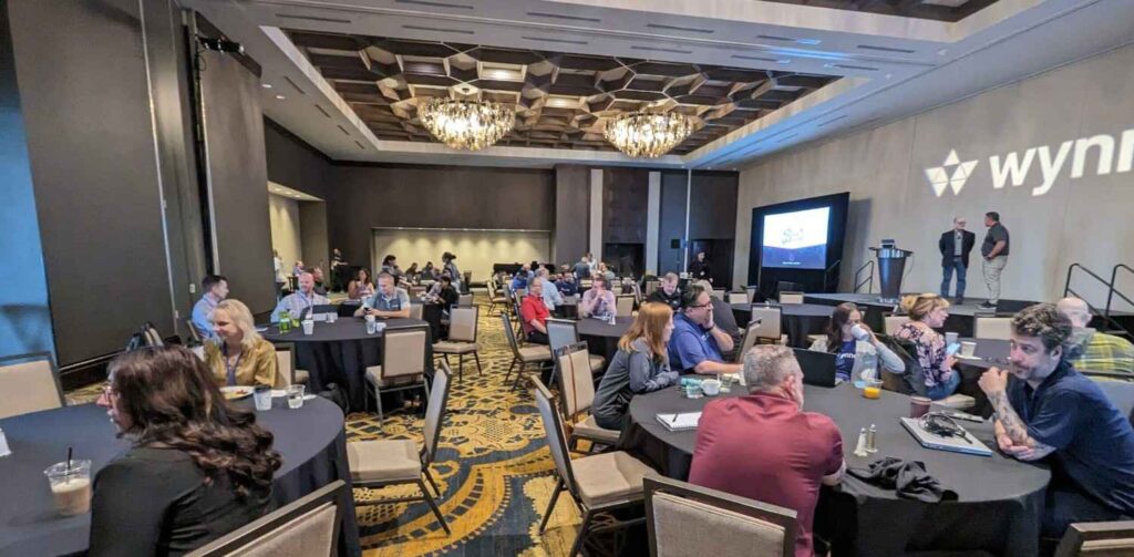 PXL 20231108 151315309 Attendees seated at tables in a large conference room during a business event with a stage and presentation screen