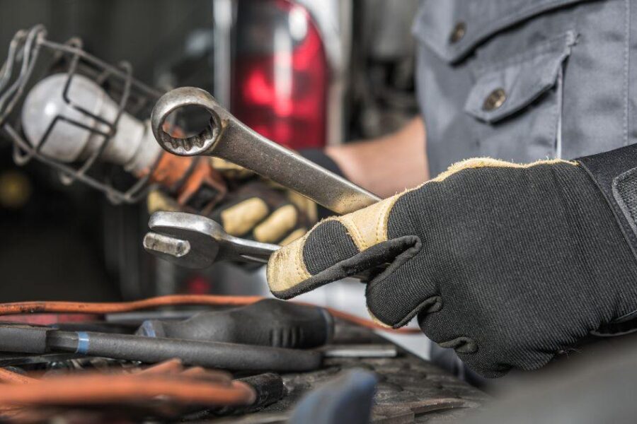 Service tech hold a wrench and light to inspect a mechanical issue