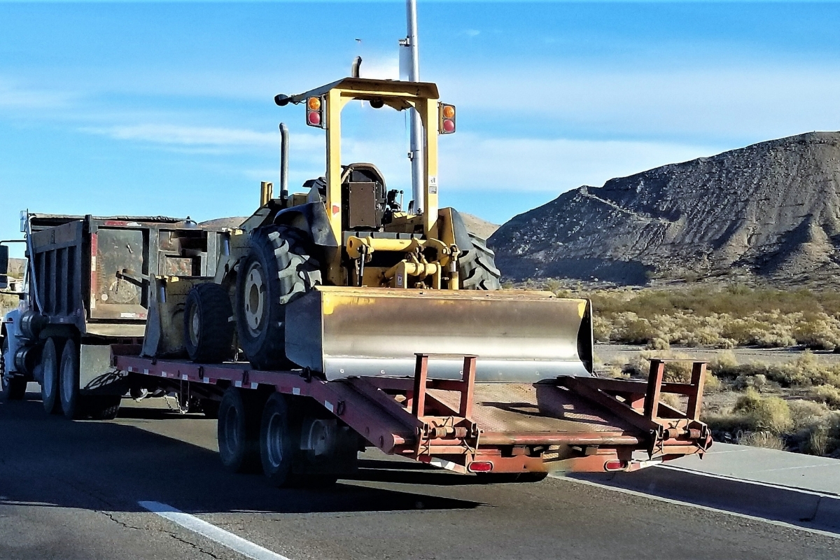 Bulldozer on trailer transported by dump truck using fleet dispatch and logistics software