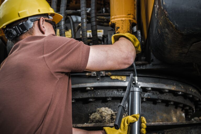 Technician greasing heavy equipment as part of equipment service management workflow.