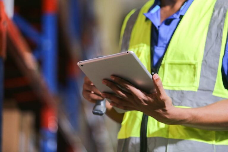 Worker in a safety vest using a tablet to check rental inventory